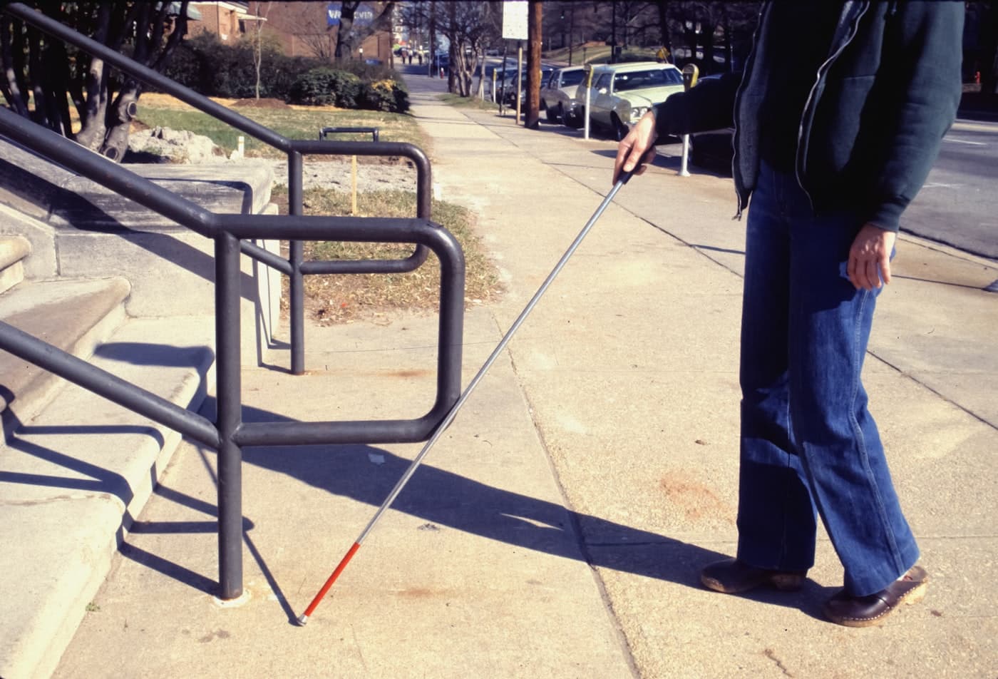 A visually impaired person using a white cane to navigate outdoor stairs, representing orientation, mobility, and practical skills training